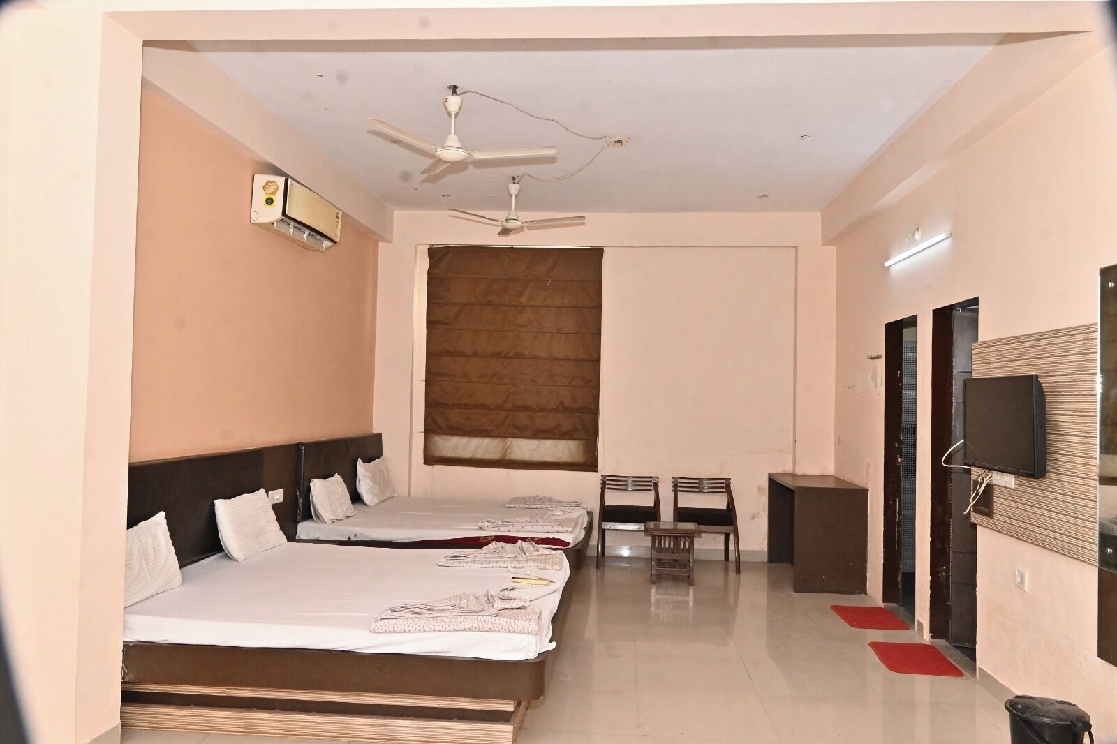 A hotel room with two beds, a ceiling fan, a TV mounted on the wall, and a small table with chairs.