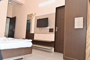A bedroom with a bed, a TV mounted on the wall, a mirror, and a door. - BANSHIDHAM DHARMASALA (Danta Ramgarh)