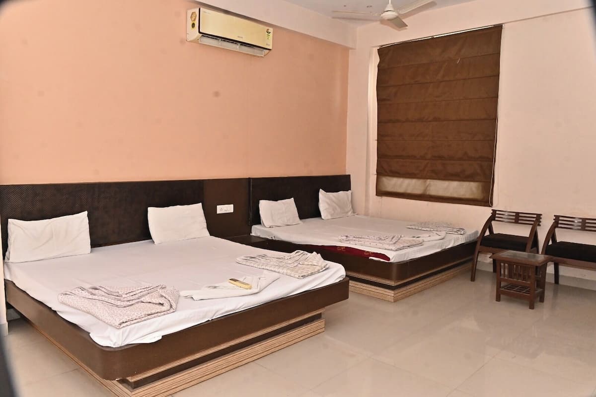 Habitación de hotel con dos camas, un ventilador de techo, un equipo de aire acondicionado, una ventana con persiana marrón y una pequeña silla de madera.