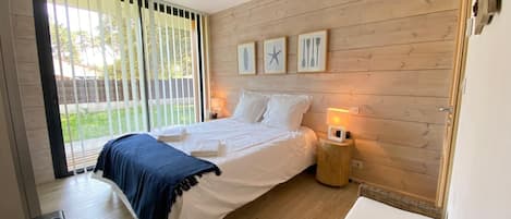 A bedroom with a bed, a nightstand, a window with blinds, and a wooden wall.