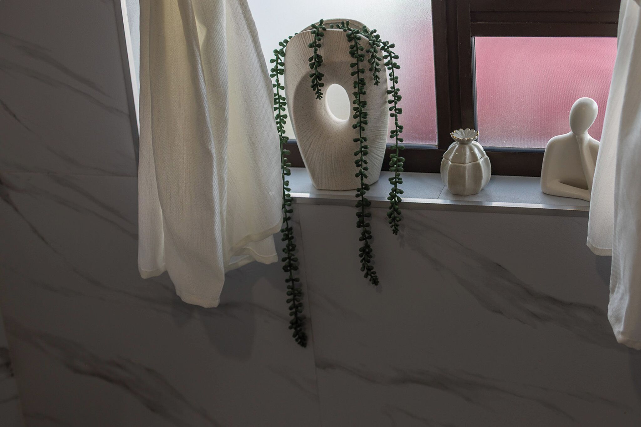Un bagno con una parete in marmo, un vaso grande con piante verdi, un piccolo vaso di fiori e una statua.