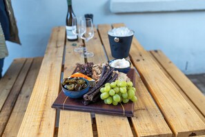 Uma mesa de madeira com diversos alimentos, incluindo uvas, azeitonas e carnes curadas.