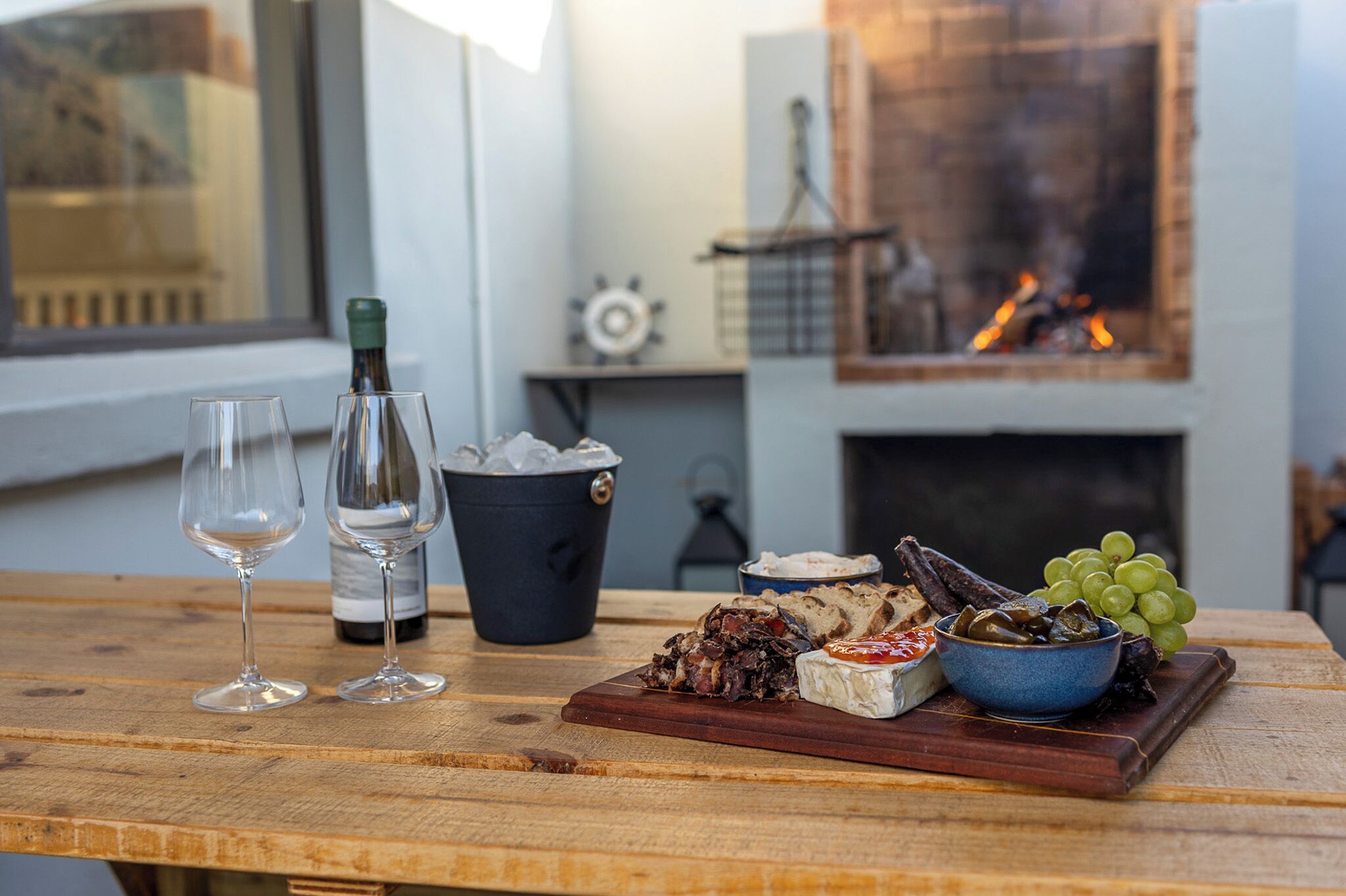 Une table en bois, une bouteille de vin, deux verres, un bol de raisins et une planche en bois sur laquelle sont disposés des aliments.
