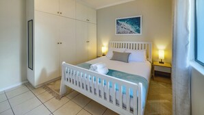 Une chambre à coucher bien rangée, avec un lit, des lampes de chevet, une armoire blanche et un tableau encadré au mur.