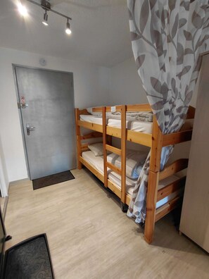 Ein Zimmer mit Etagenbett, einer verschließbaren Tür, einem Lichtschalter und einer kleinen Fußmatte.