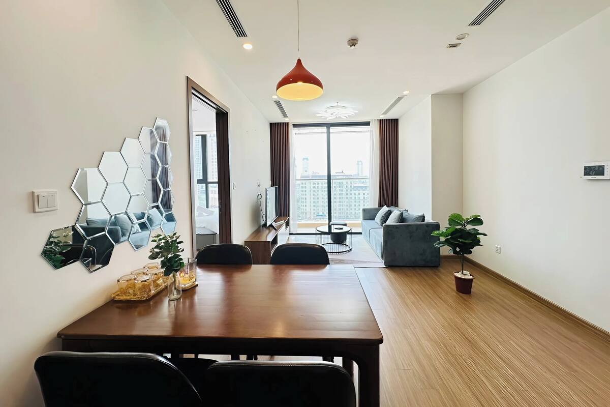 Un salon moderne avec une table à manger en bois, un canapé et une grande fenêtre donnant sur la ville.