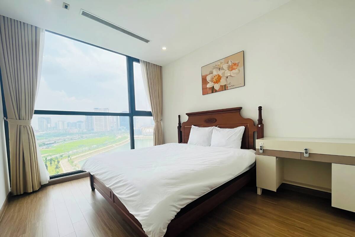 Une chambre d’hôtel avec un grand lit, une table de chevet, une commode, une fenêtre avec des rideaux et un tableau au mur.