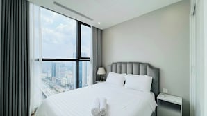A modern hotel room with a large bed, a nightstand, a lamp, and a view of the city through large windows. - Vinhome Sky Lake-Sunhometel (Hanoi)