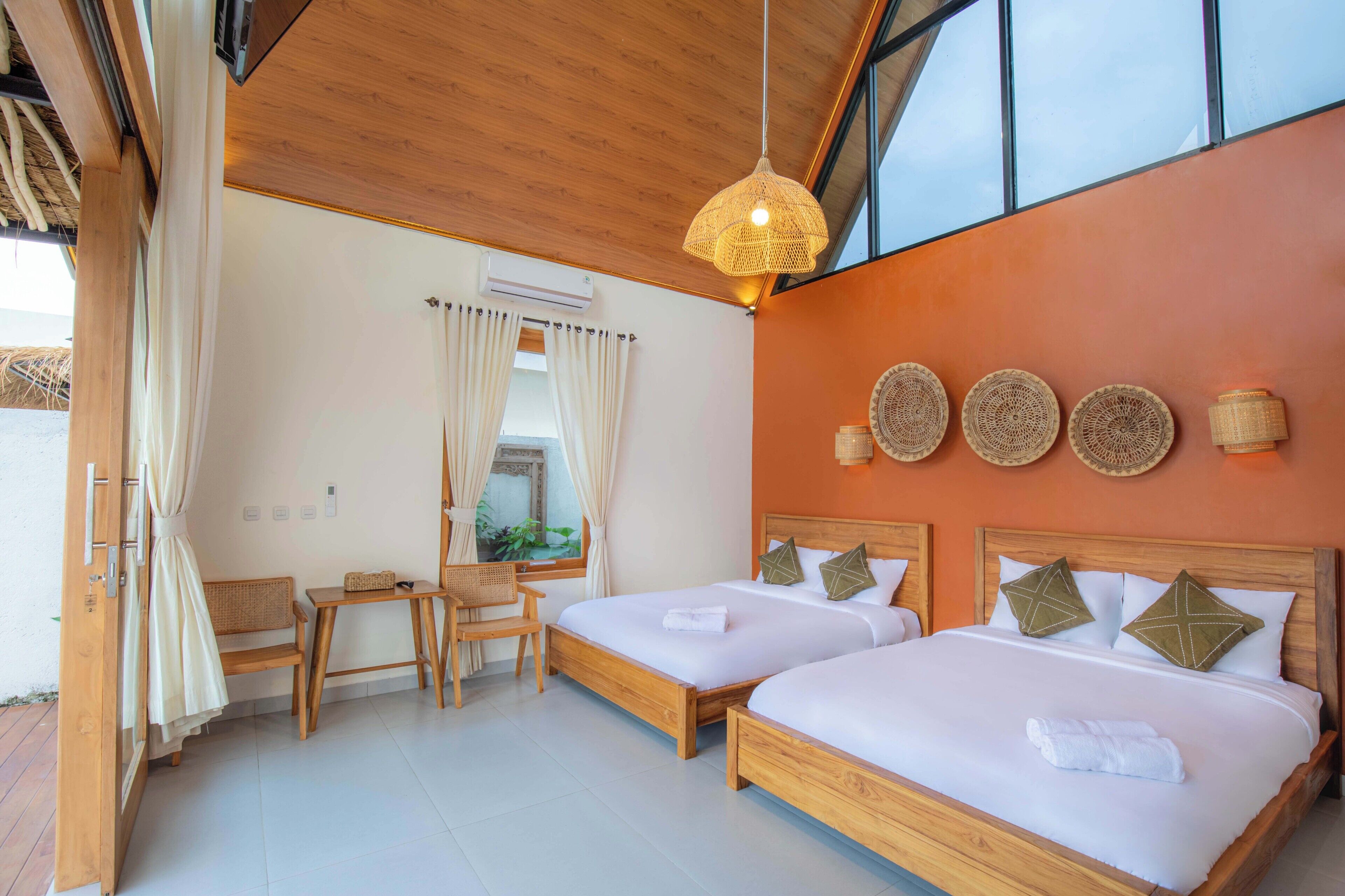 Une chambre d’hôtel moderne avec deux lits en bois, un petit coin salon et une grande fenêtre.
