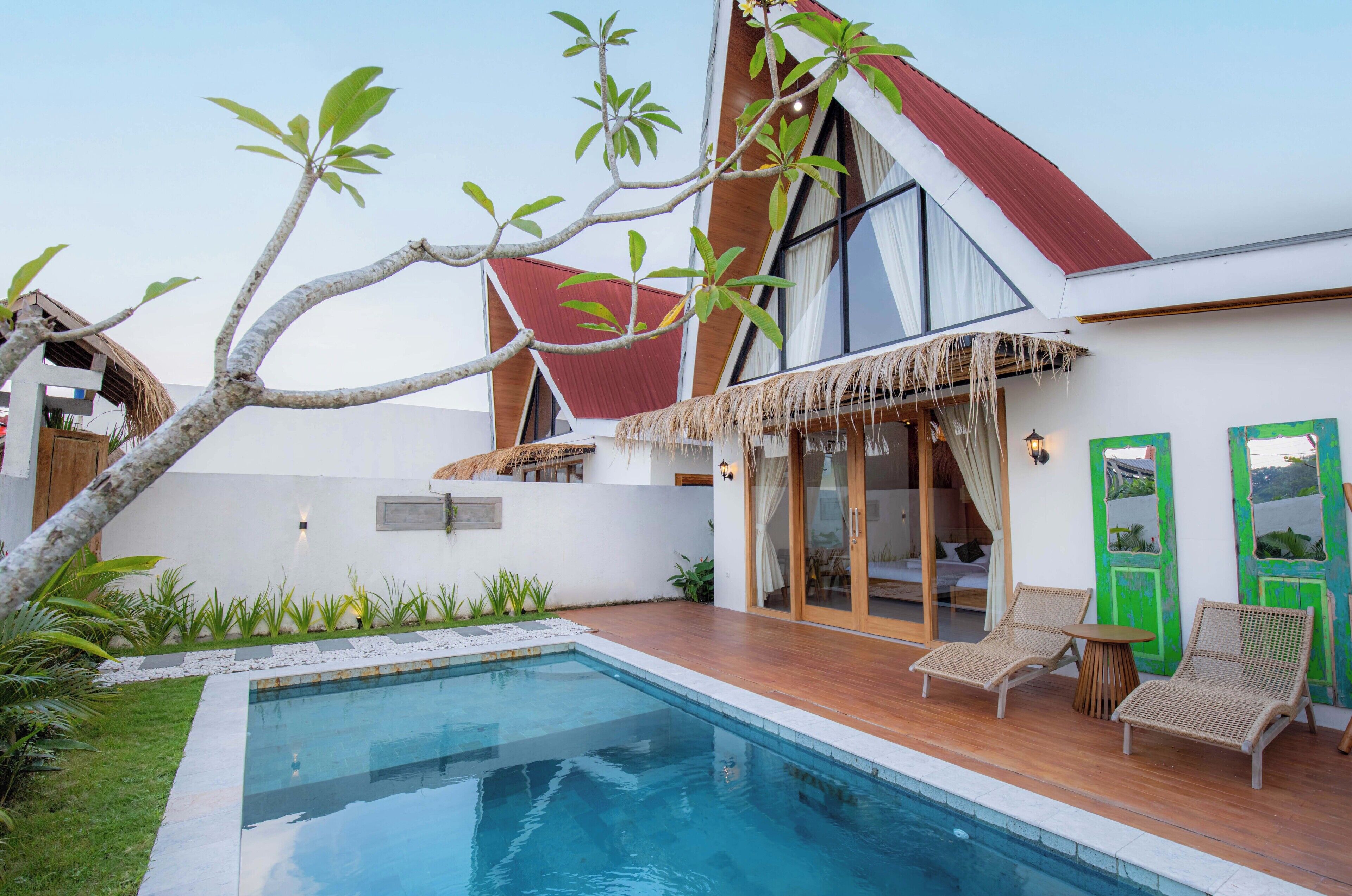 A modern house with a swimming pool, two lounge chairs, and a thatched roof.