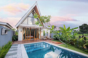 Ein modernes Haus mit Pool, großen Fenstern und einem tropischen Garten.