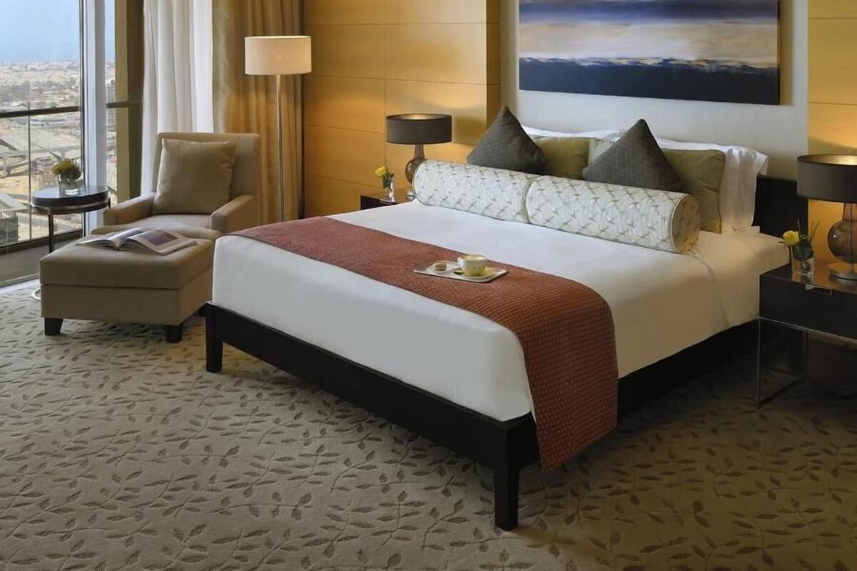 A hotel room with a large bed, a chair, a bedside table, a lamp, and a painting on the wall.