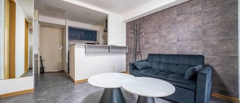A modern living room with a dark grey sofa, two round tables with white tops, and a grey tiled wall.
