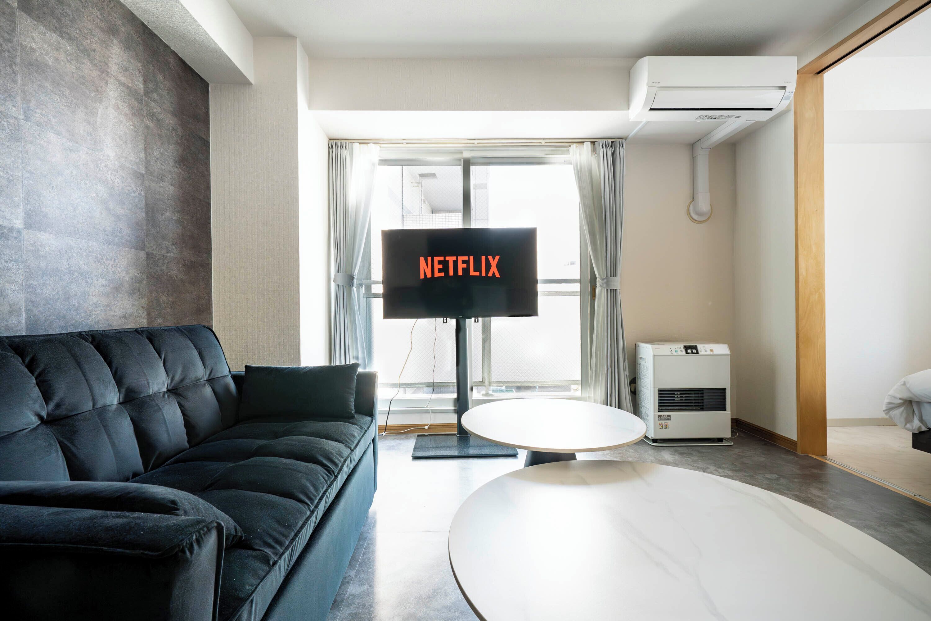 A modern living room with a black leather sofa, a round white table, and a TV displaying "NETFLIX".