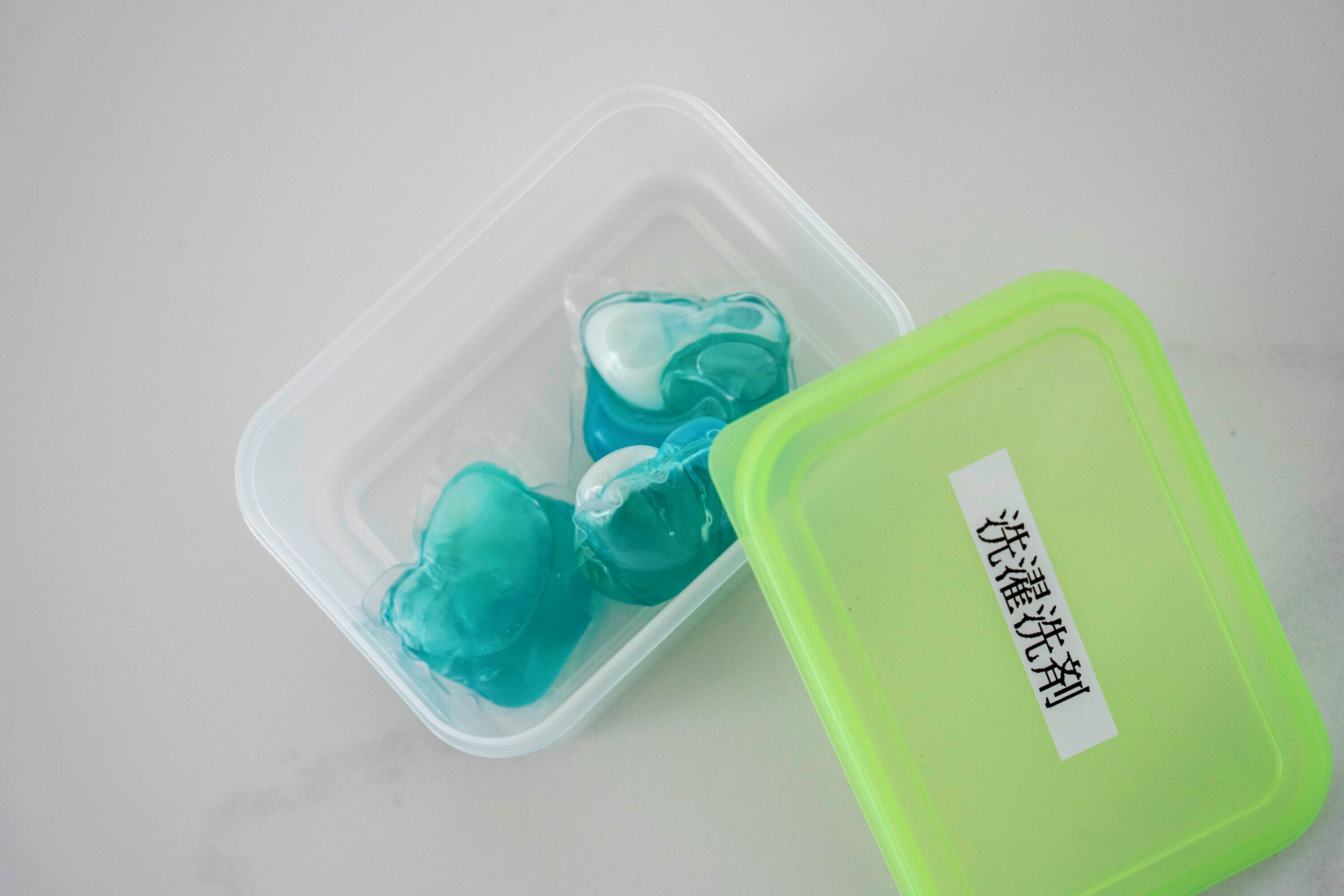 A clear plastic container with a green lid, containing three blue ice cubes.