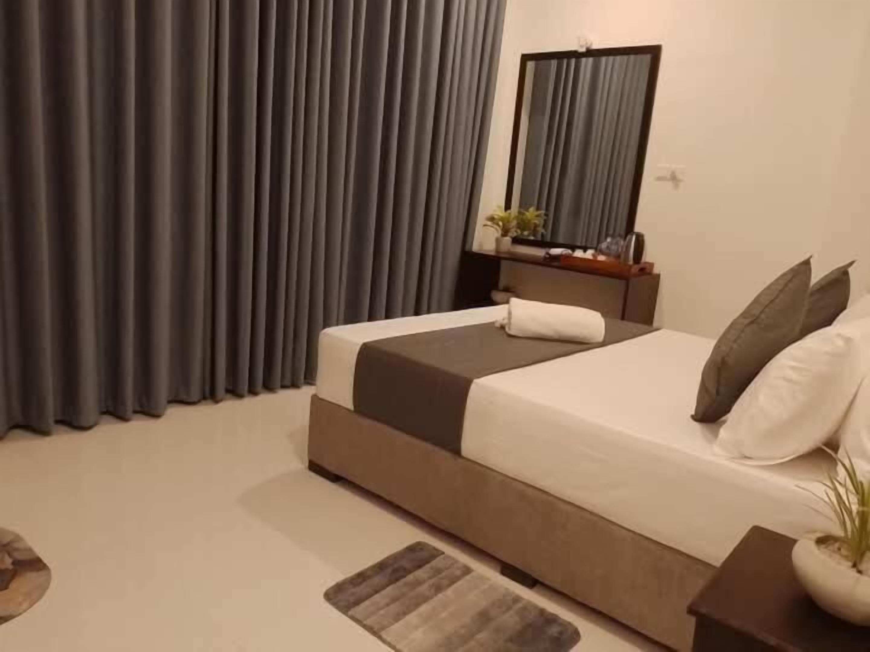 Quarto com cama, cortinas, espelho, mesa de cabeceira e uma pequena planta.