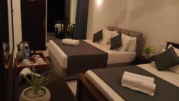 A hotel room with two beds, a small table with a kettle and a tray, a potted plant, and a nightstand with a lamp.