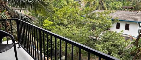 A balcony with a view of a lush garden and a white building with a red roof.