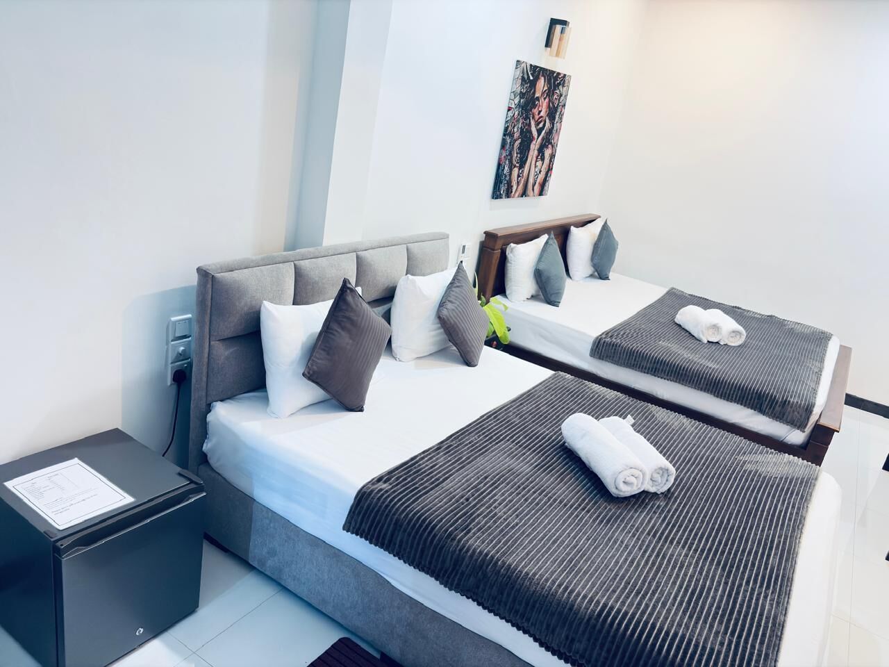 Een hotelkamer met een groot bed, een kleiner bed, een nachtkastje en een kunstwerk aan de muur.
