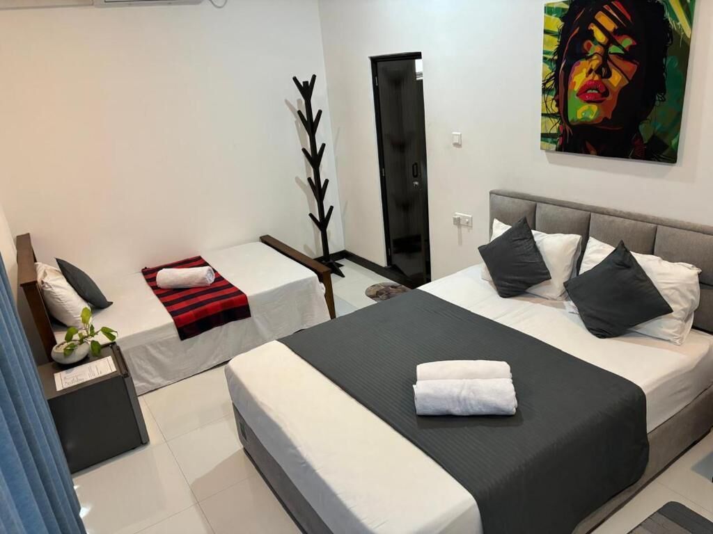 A modern hotel room with a large bed, a separate sofa, a desk, and a door leading to a bathroom.
