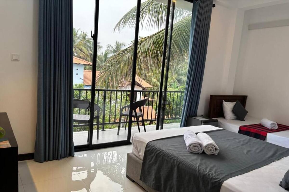 A hotel room with a balcony, a bed with a dark bedspread, a nightstand, and a chair.