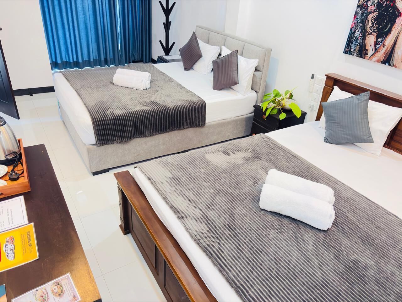 Une chambre d’hôtel avec deux lits, un bureau, une chaise, une plante et un tableau au mur.