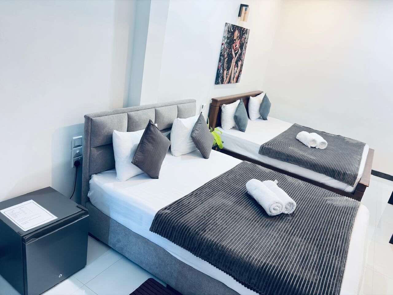 Hotellihuone, jossa on kaksi sänkyä, yöpöytä, pieni työpöytä ja seinälle ripustettu taideteos.