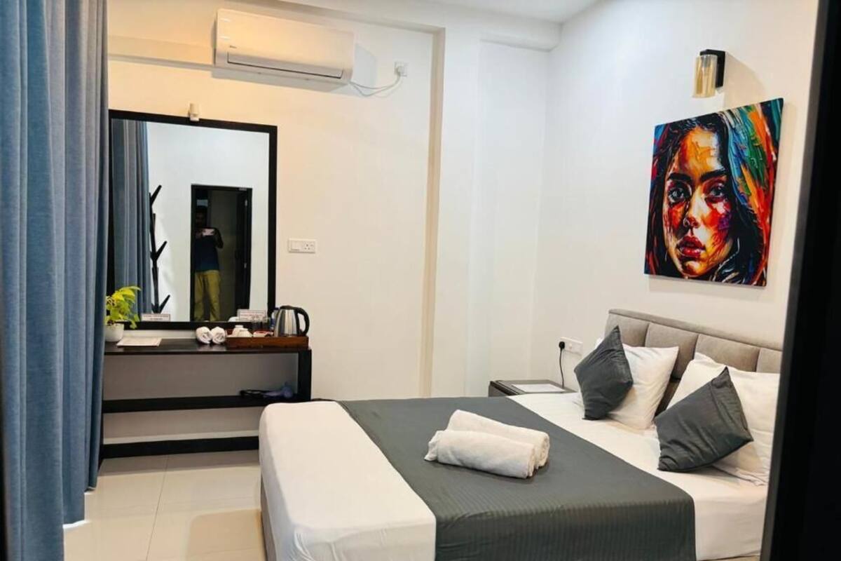 A modern hotel room with a bed, a bedside table, a mirror, a painting, and a window.