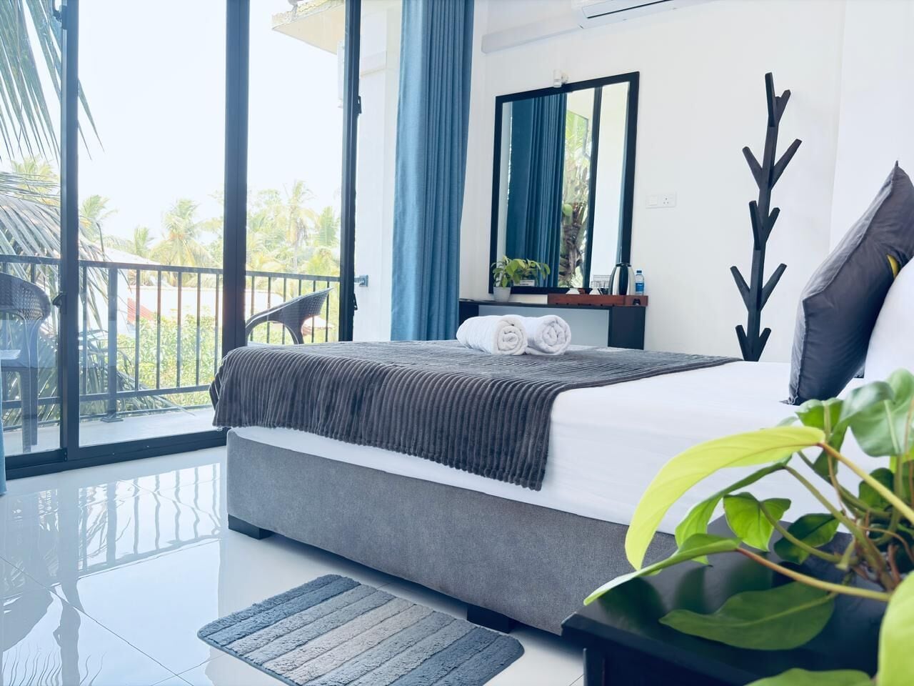 A modern bedroom with a large bed, a balcony with a chair, a mirror, and a plant.