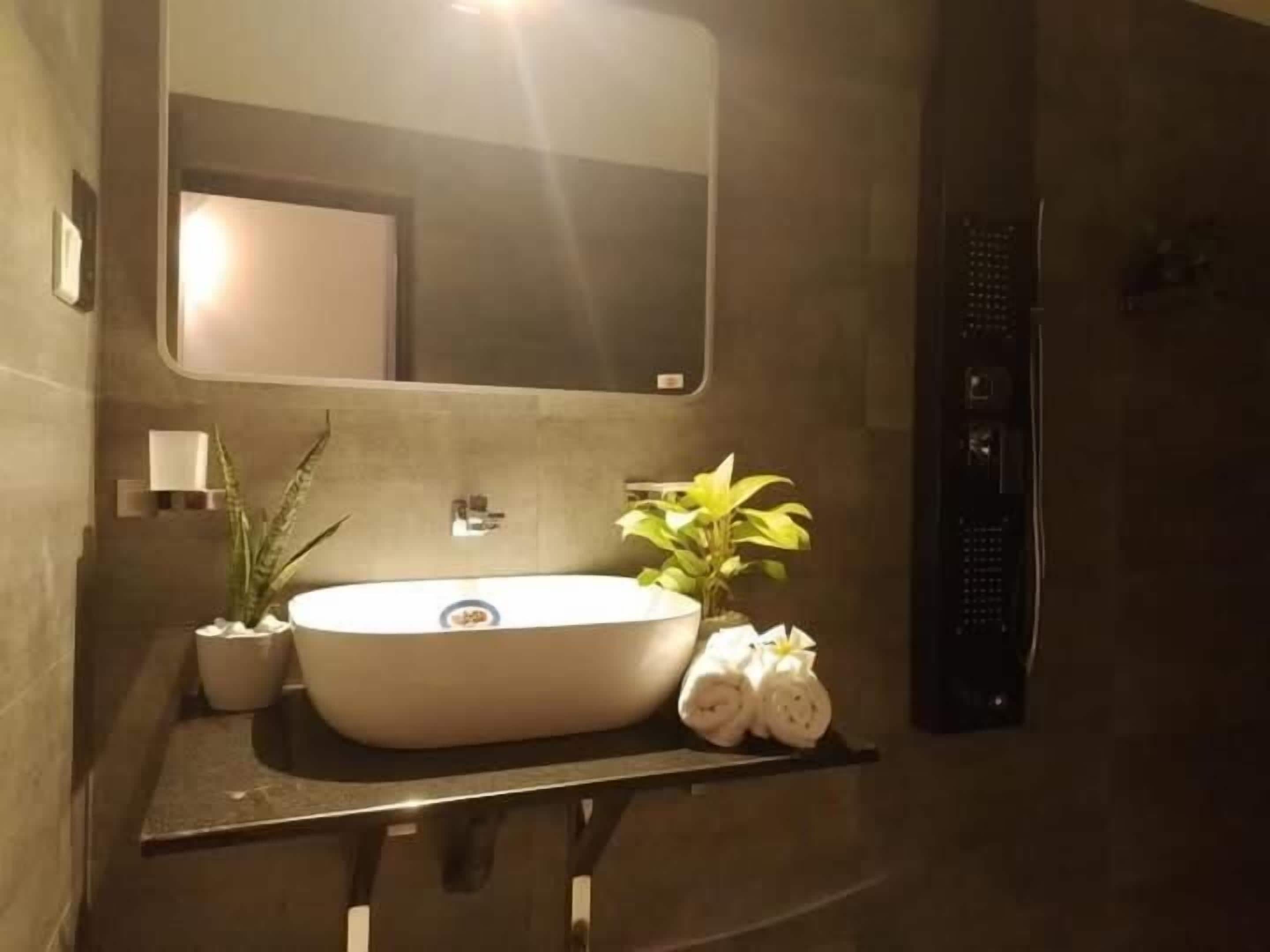 Un baño con un espejo grande, un lavabo, una planta en maceta y toallas.