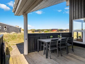 A wooden deck with a table and chairs, overlooking a coastal landscape with buildings in the distance.
