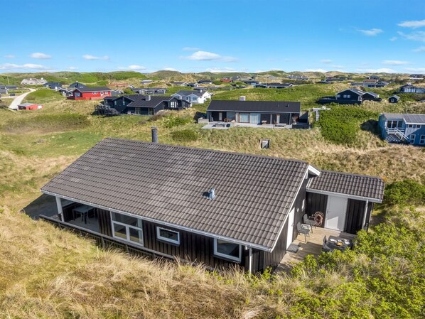A modern house with a sloped roof, a deck, and a view of a coastal landscape.