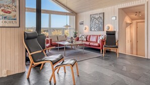 Un salon spacieux avec une grande fenêtre, un canapé en cuir rouge, un fauteuil en cuir noir et une table basse en bois.