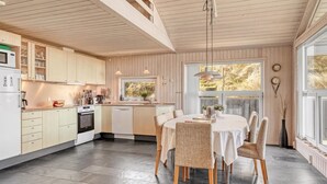 Une cuisine moderne avec des meubles en bois, un coin repas doté d’une table ronde et de chaises, et de grandes fenêtres qui laissent entrer la lumière naturelle.