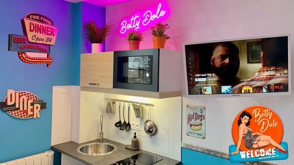 A modern kitchen with a neon sign reading "Betty Dole," a microwave, and a TV displaying a movie.