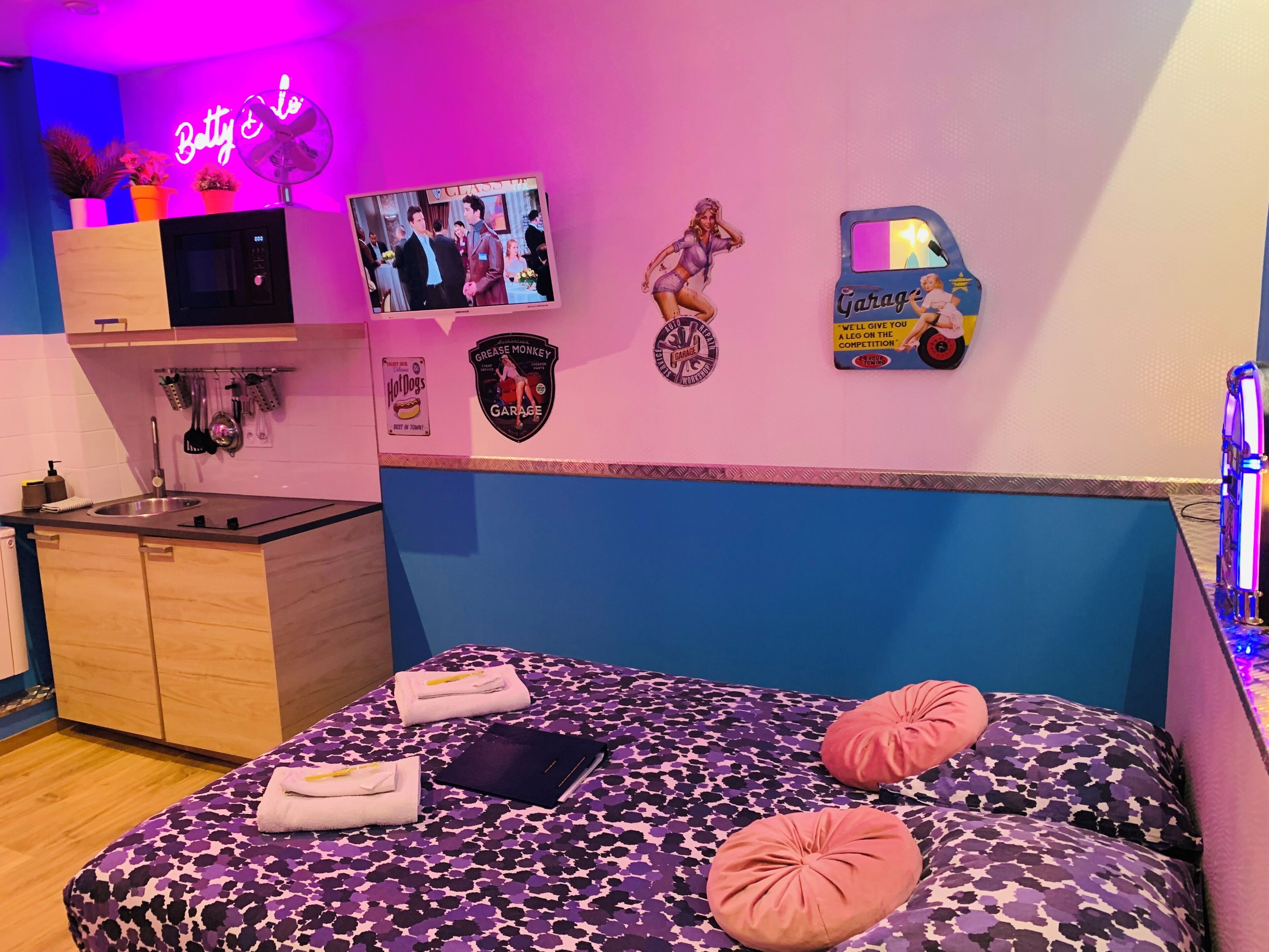Un dormitorio con una cama, un televisor, un letrero de neón y una pared decorada con pegatinas.