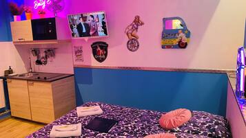 Un dormitorio con una cama, un televisor, un letrero de neón y una pared decorada con pegatinas.