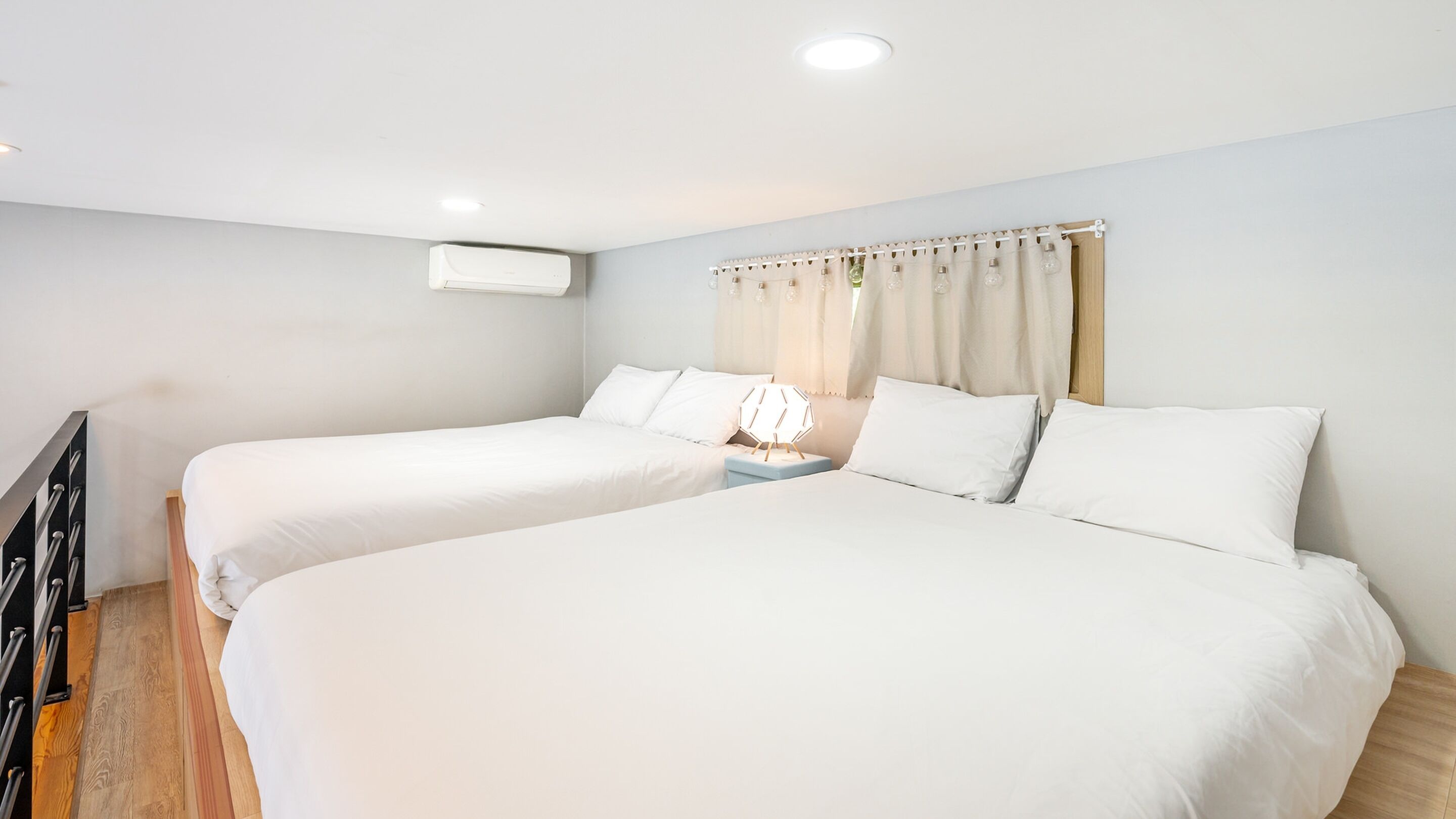 A double bed room with white bedding, a bedside table, and a wall-mounted air conditioner.