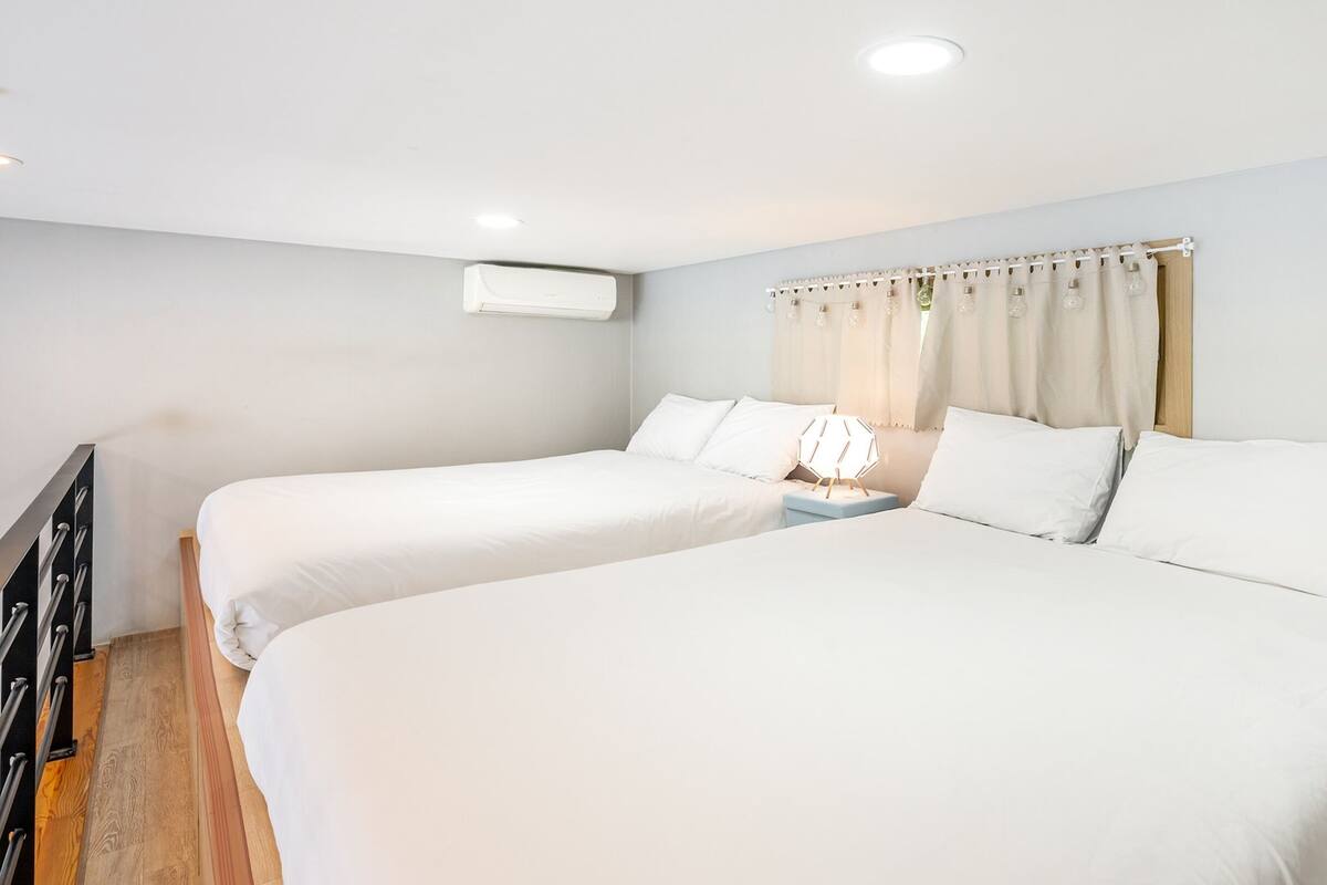 Ein Doppelzimmer mit weißer Bettwäsche, einem Nachttisch und einer Wand-Klimaanlage.