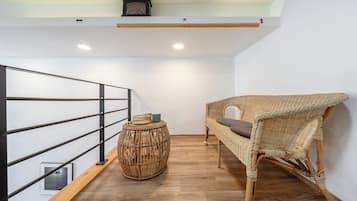 Quarto nos fundos com uma cadeira de vime, uma mesinha redonda com um tabuleiro e um corrimão de metal.