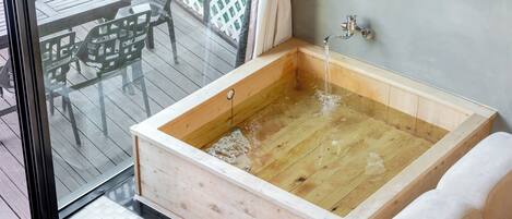Un bain à remous en bois, doté d’un robinet, d’une porte en verre et d’une terrasse en bois avec des chaises.