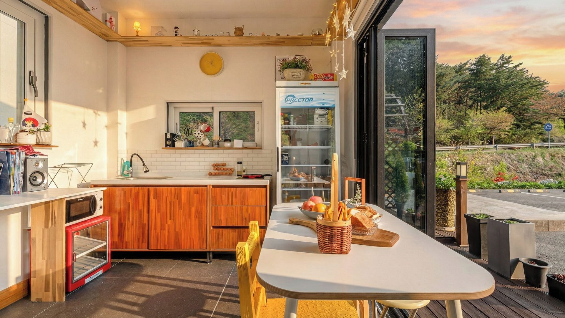 Uma cozinha compacta com geladeira embutida, uma mesa de jantar com cadeiras e vista para o exterior através de uma porta de vidro.