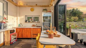 Uma cozinha compacta com geladeira embutida, uma mesa de jantar com cadeiras e vista para o exterior através de uma porta de vidro.