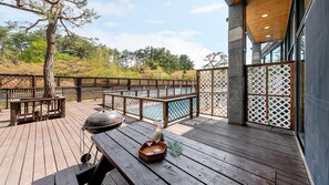 Un terrazzo in legno con una griglia barbecue e un tavolo apparecchiato per due, con vista su una zona piscina.