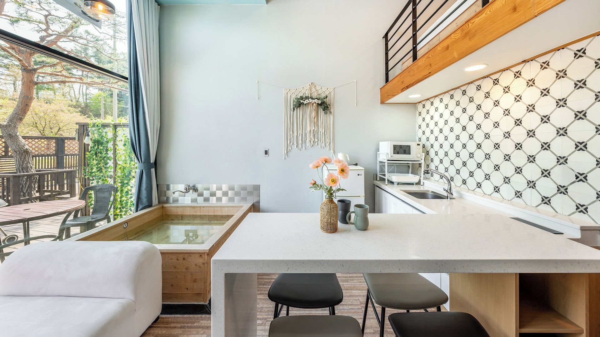 Una cocina moderna con una isla central, una zona de comedor con un sofá blanco y vistas al exterior.