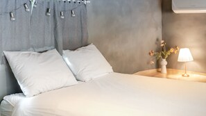 A neatly made bed with white linens, a grey headboard with light fixtures, and a bedside table with a lamp and a vase of flowers. - Gangneung Awesome Pension (Gangneung)