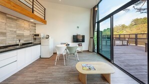 A modern kitchen with white cabinets, a microwave, and a refrigerator. There is a dining area with a table and chairs, and a large window offering a view of the outdoors. - Gangneung Awesome Pension (Gangneung)