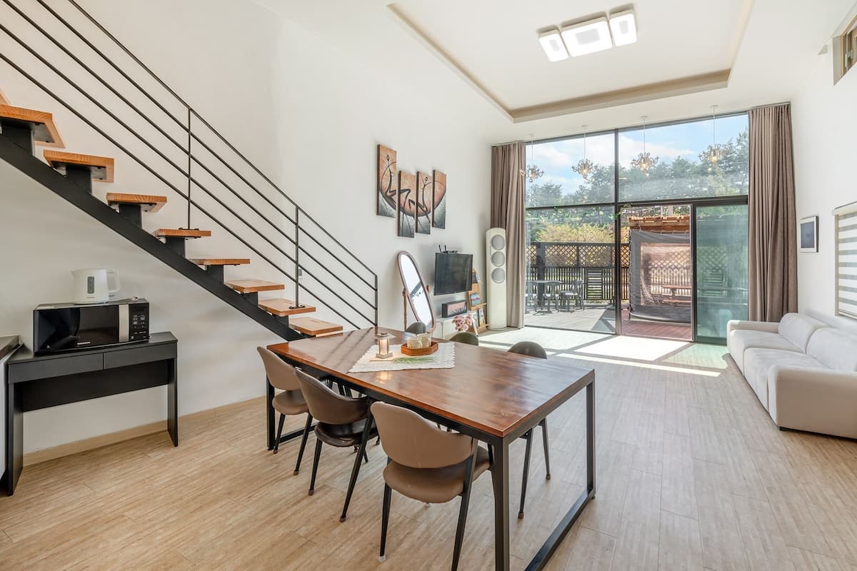 Ein modernes Wohnzimmer mit Essbereich, einer Treppe, einer Couch und einer großen Glasschiebetür, die auf eine Terrasse im Freien führt.
