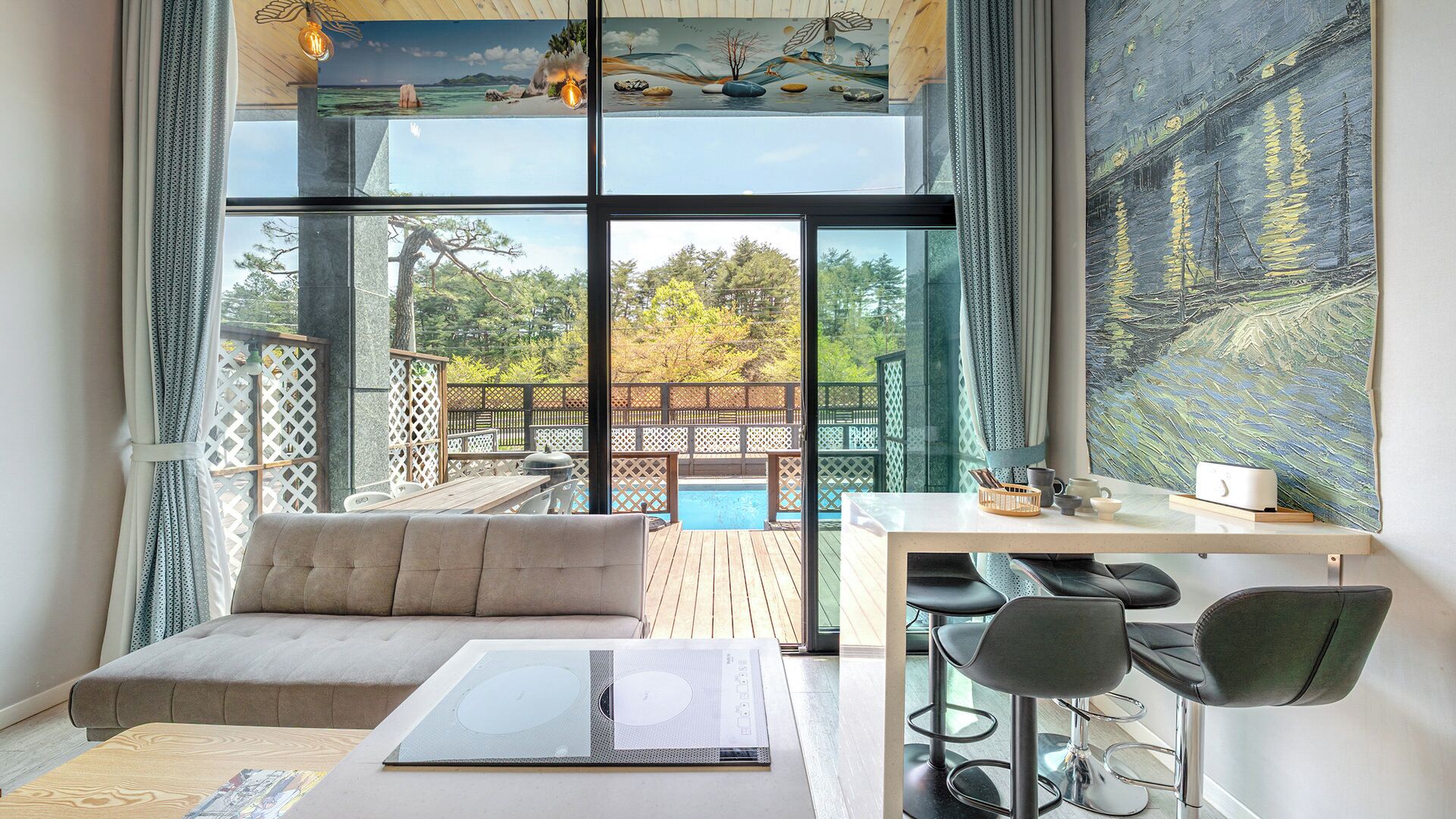 Una habitación moderna con un ventanal grande, un sofá, una mesa con sillas y vistas a una piscina y zona exterior.