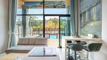 Una habitación moderna con un ventanal grande, un sofá, una mesa con sillas y vistas a una piscina y zona exterior.